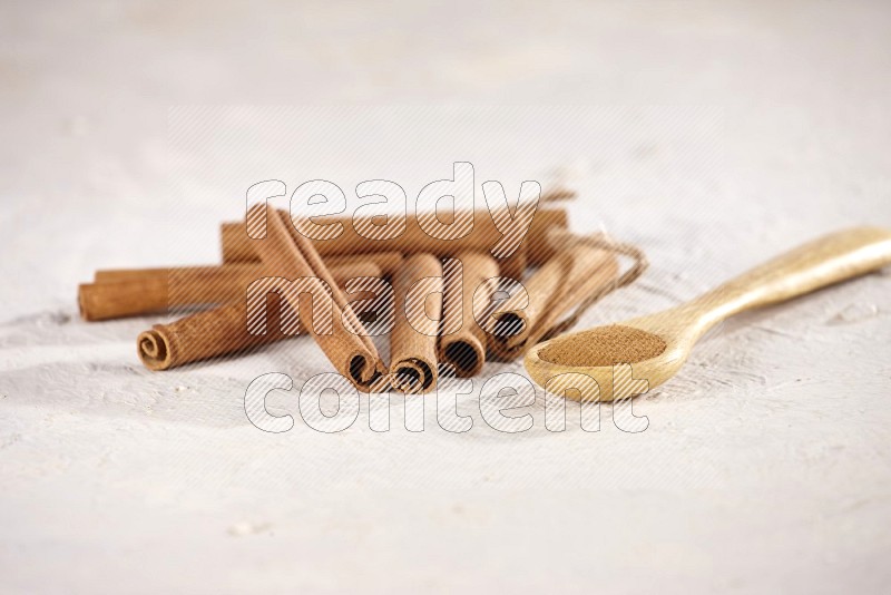 Cinnamon sticks stacked beside a wooden spoon full of cinnamon powder on white background