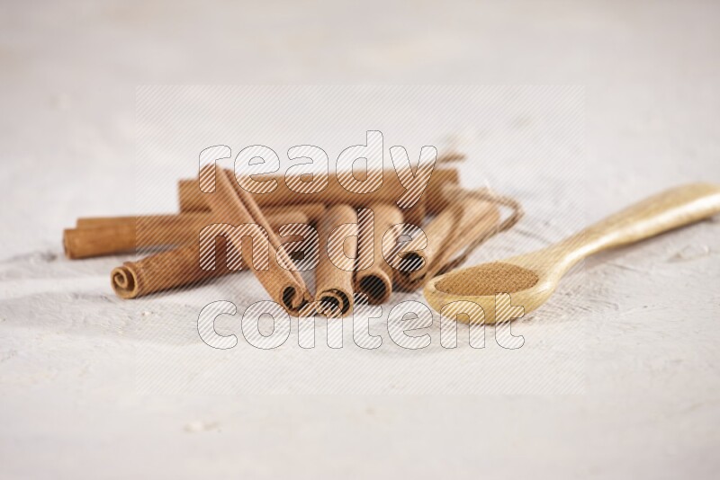 Cinnamon sticks stacked beside a wooden spoon full of cinnamon powder on white background