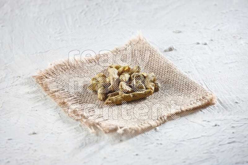 Dried turmeric whole fingers on a piece of burlap on a textured while flooring