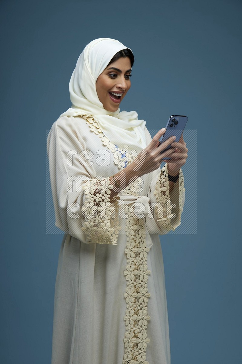 A Saudi woman Texting in a blue background wearing an off-white Abaya Hijab