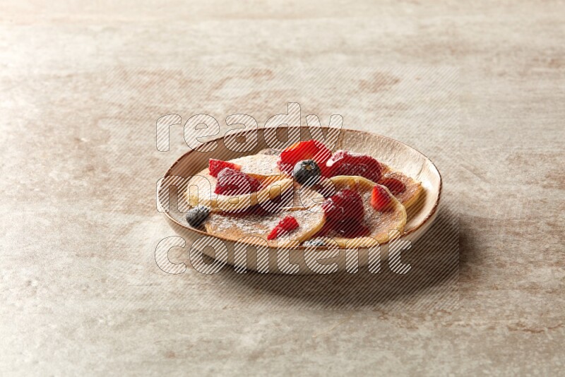 Five stacked mixed berries mini pancakes in an irregular plate on beige background