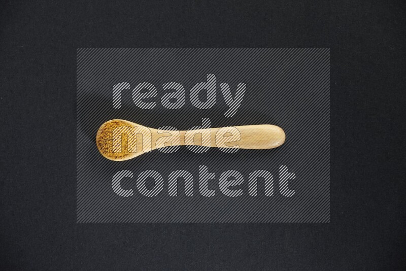 A wooden spoon full of turmeric powder on black flooring