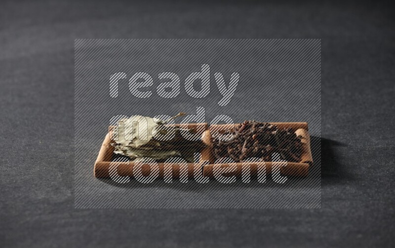 مربعان من أعواد القرفة ممتلئان بالقرنفل وأوراق الغار علي خلفية سوداء