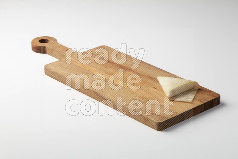 One uncooked samosa on a wooden cutter on a white background