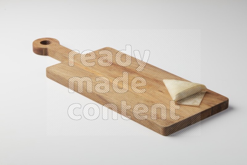 One uncooked samosa on a wooden cutter on a white background