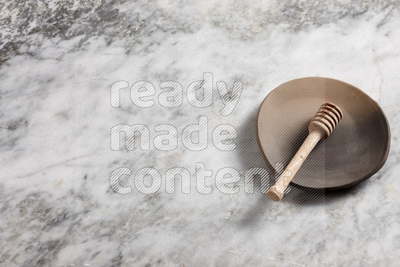 Multicolored Pottery Plate with wooden honey handle in it, on grey marble flooring, 65 degree angle