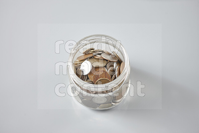 Random old coins in a glass jar on grey background