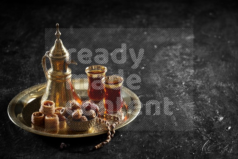 Oriental sweets with dates and a drink on a metal tray in a dark setup