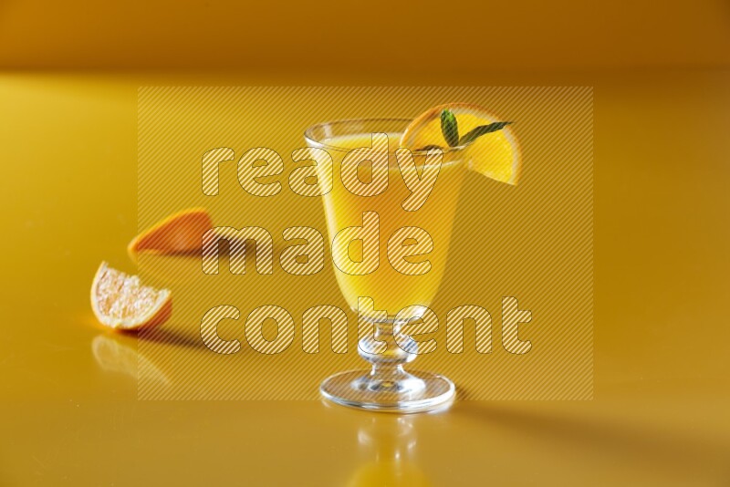 glass of orange juice with orange & mint  on yellow background