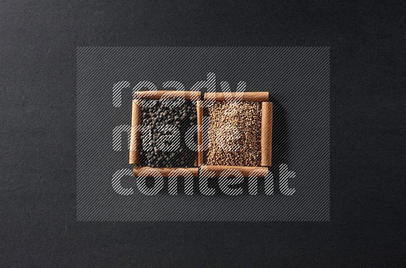 مربعان من أعواد القرفة ممتلئان بحبوب الخردل وحبوب الفلفل الأسود علي خلفية سوداء