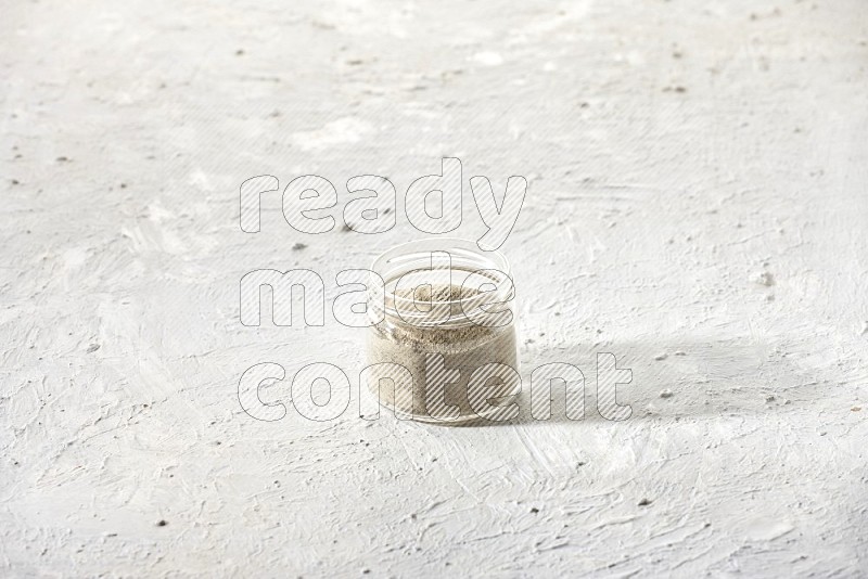 وعاء زجاجي ممتلئ ببودرة الفلفل الأبيض على أرضية بيضاء