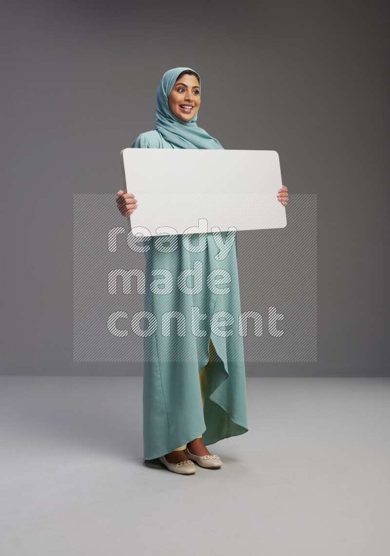 Saudi Woman wearing Abaya standing holding board on Gray background