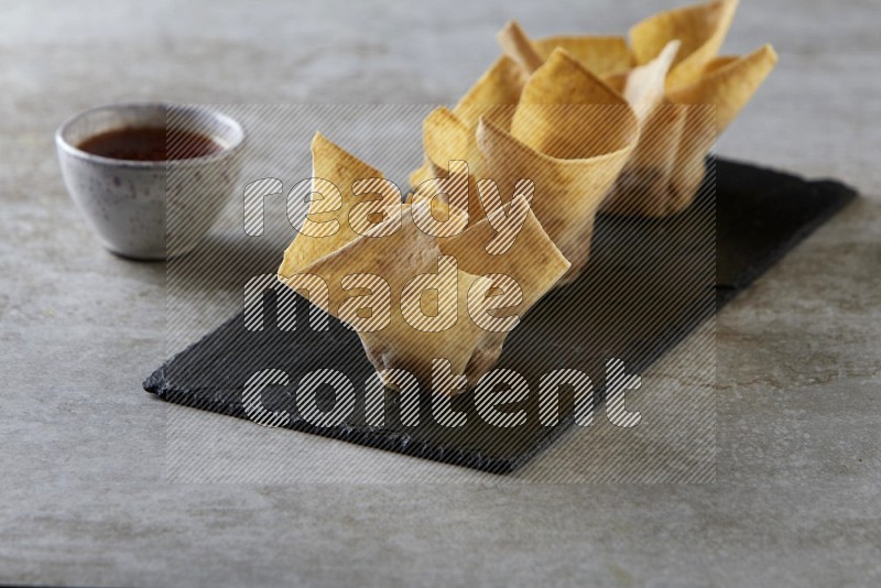 wonton cups with soy sauce ramkin on rectangle slate on grey textured counter top