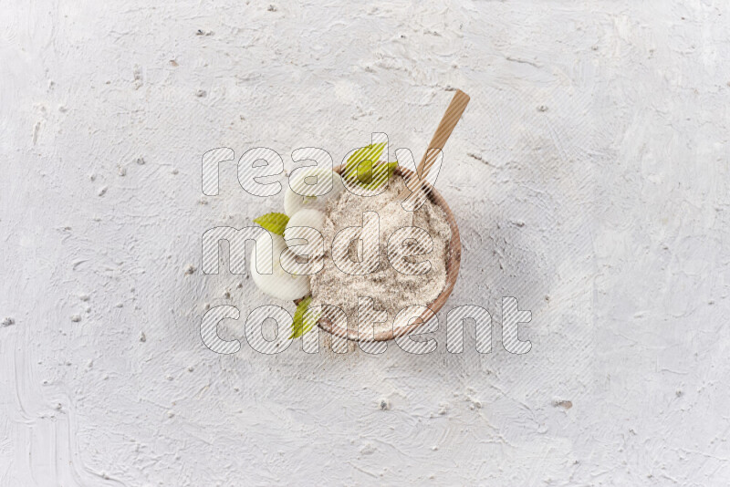 A wooden bowl full of onion powder with a wooden spoon in it with some sliced onions on white background