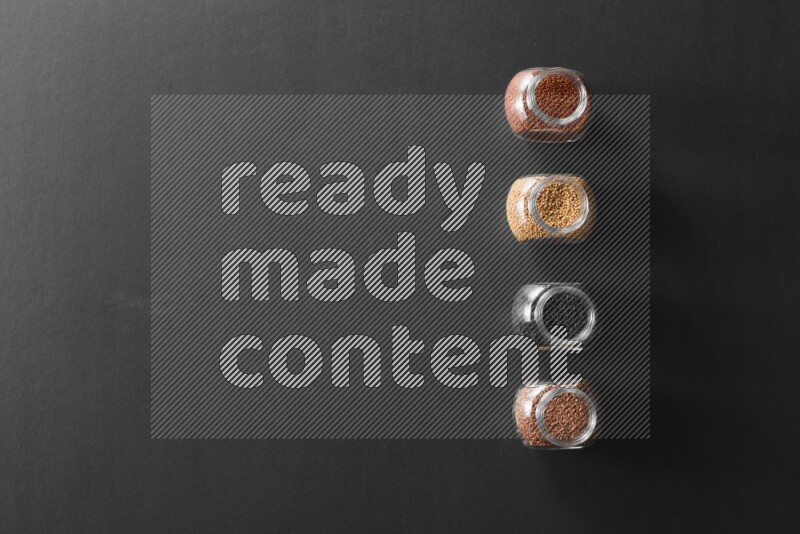 4 glass spice jars full of black seeds, mustard seeds, flax and garden cress on black flooring