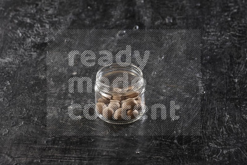 A glass jar full of whole nutmeg seeds on a black flooring