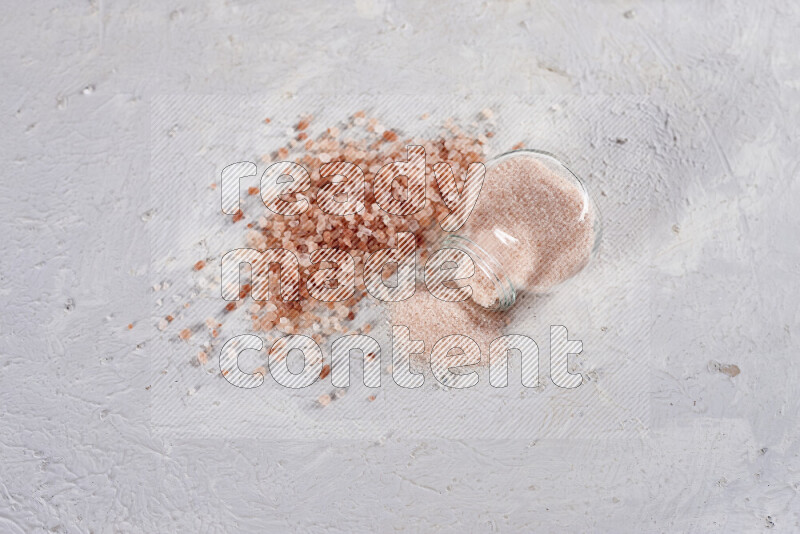 A glass jar full of fine himalayan salt with some himalayan crystals beside it on a white background