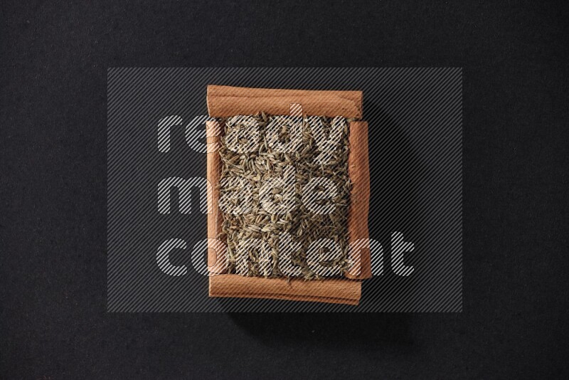A single square of cinnamon sticks full of cumin on black flooring