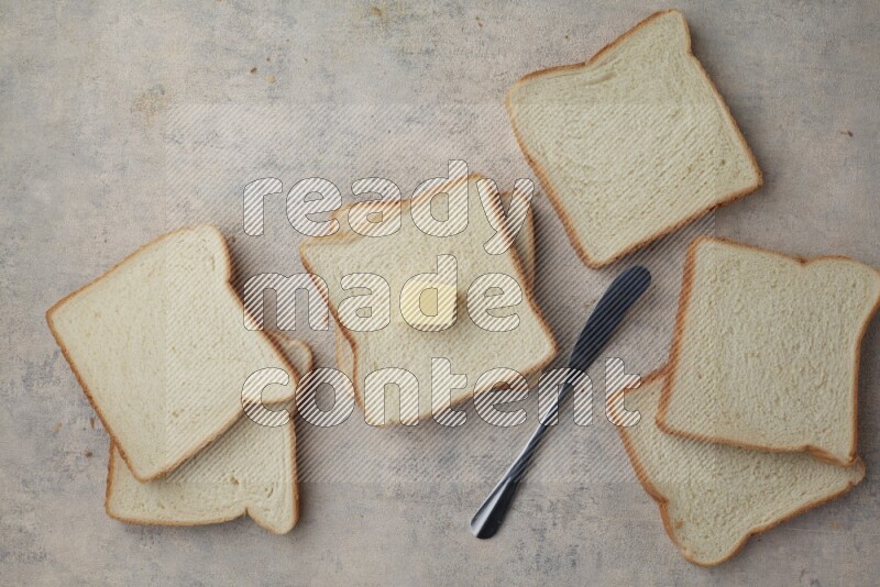 White toast slices with a butter cube and a spreading knife on a light blue textured background
