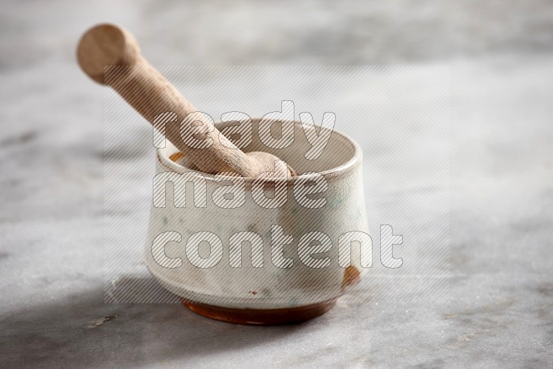 Multicolored Pottery bowl with wooden honey handle in it, on grey marble flooring, 15 degree angle