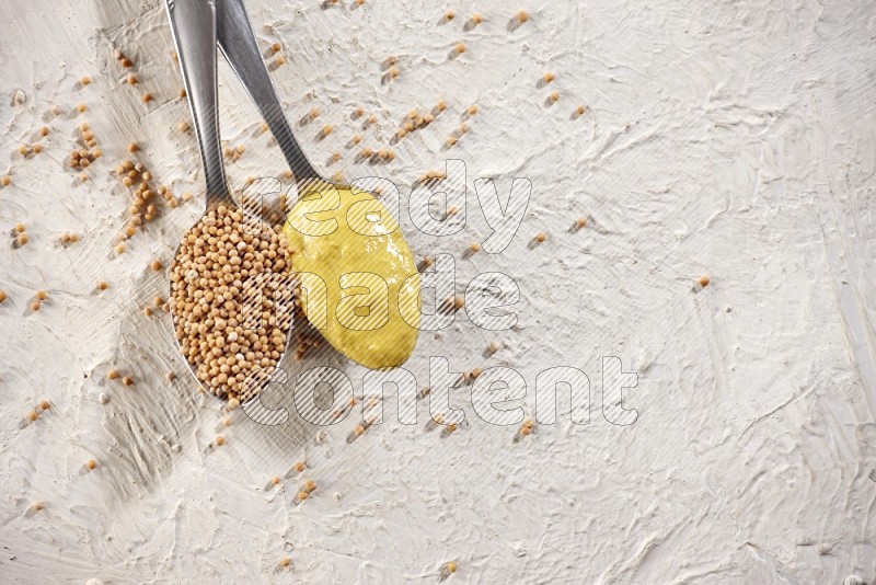 Two metal spoons, one filled with mustard seeds and the other with mustard paste on white background