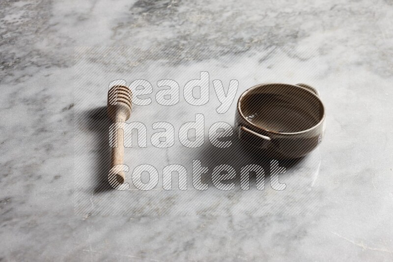 Multicolored pottery bowl with wooden honey dipper on the side on grey marble background