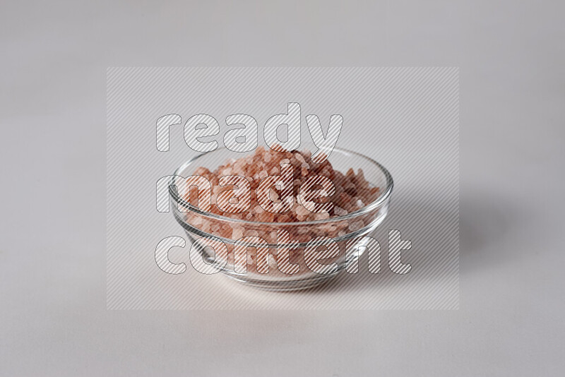 A glass bowl full of coarse himalayan salt crystals on white background