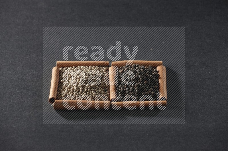 مربعان من أعواد القرفة ممتلئان بحبوب الفلفل الأبيض وحبوب الفلفل الأسود علي خلفية سوداء