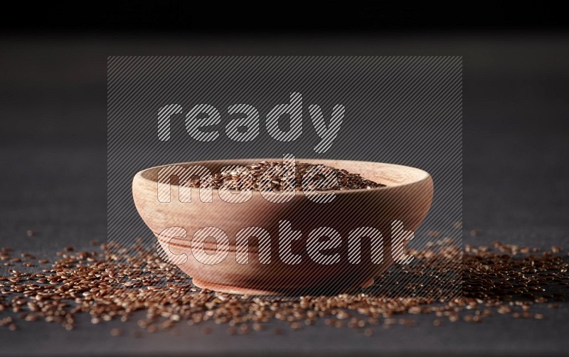 A wooden bowl full of flax surrounded by the seeds on a black flooring in different angles