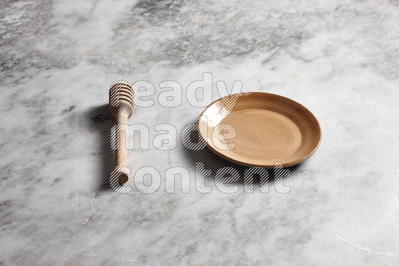 Beige Pottery Plate with wooden honey handle on the side with grey marble flooring, 45 degree angle
