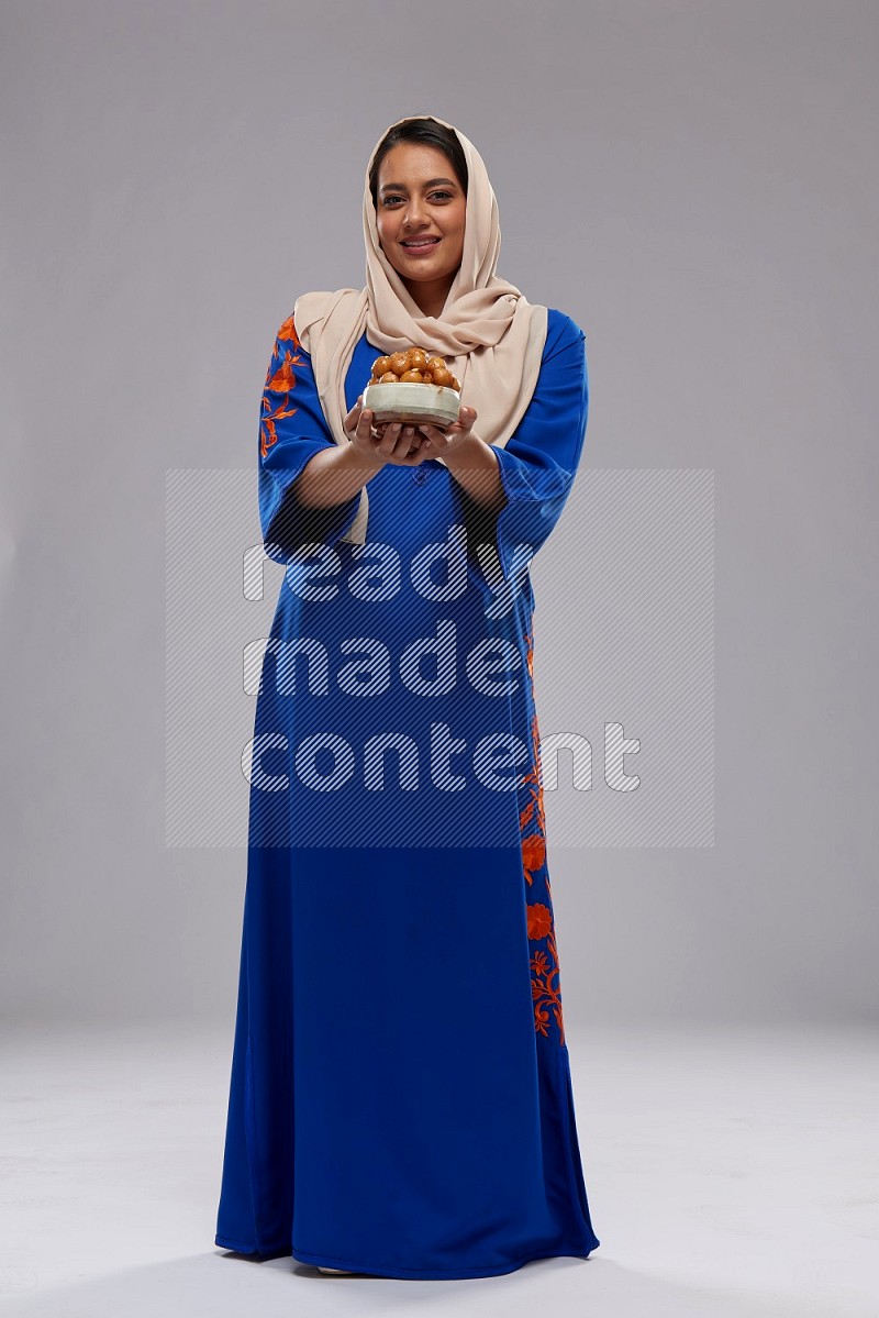 A Saudi woman standing wearing Jalabeya holding a plate of luqaimat
