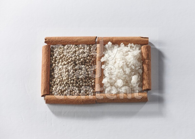 2 squares of cinnamon sticks full of white pepper and white salt on white flooring