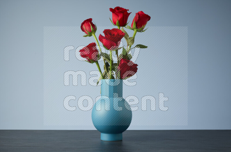 An arrangement of vivid red roses in a blue vase on black marble background