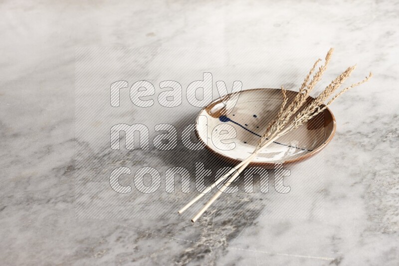 Wheat stalks on multicolored pottery plate on grey marble background