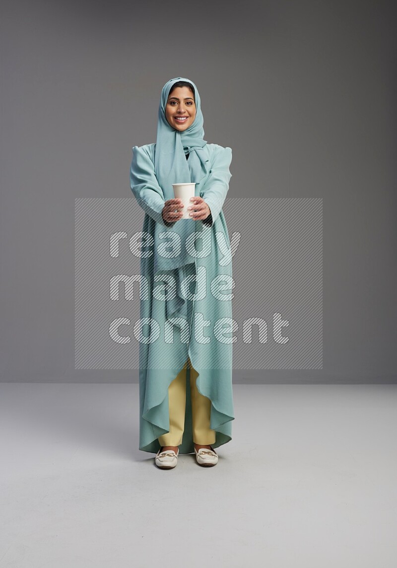 Saudi Woman wearing Abaya standing  holding paper cup on Gray background