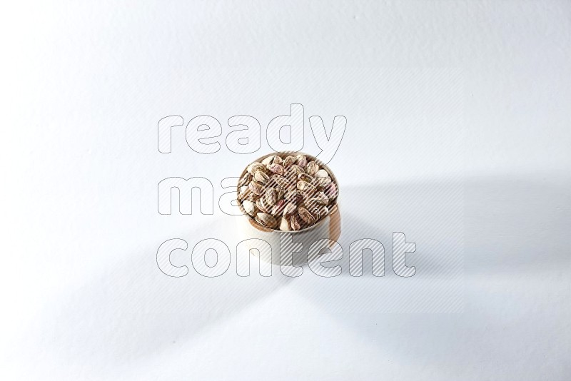 A beige ceramic bowl full of peeled pistachios on a white background in different angles