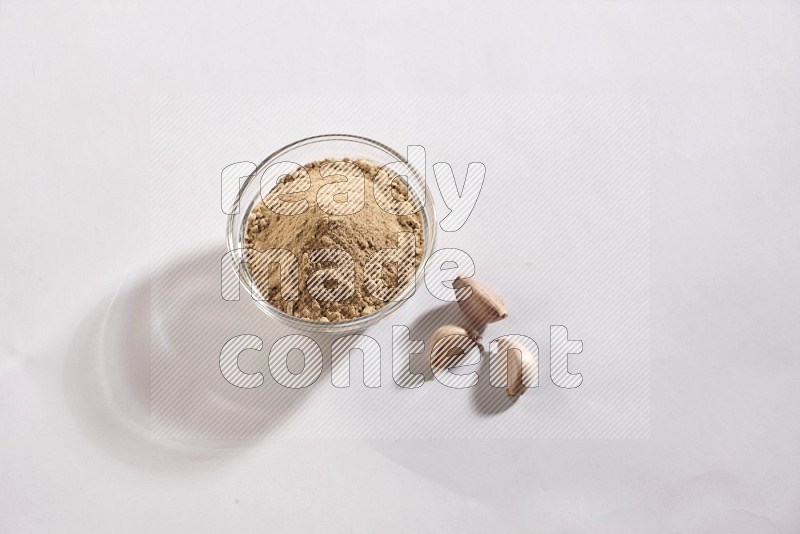 A glass bowl full of garlic powder and beside it garlic bulb and cloves on a white flooring in different angles