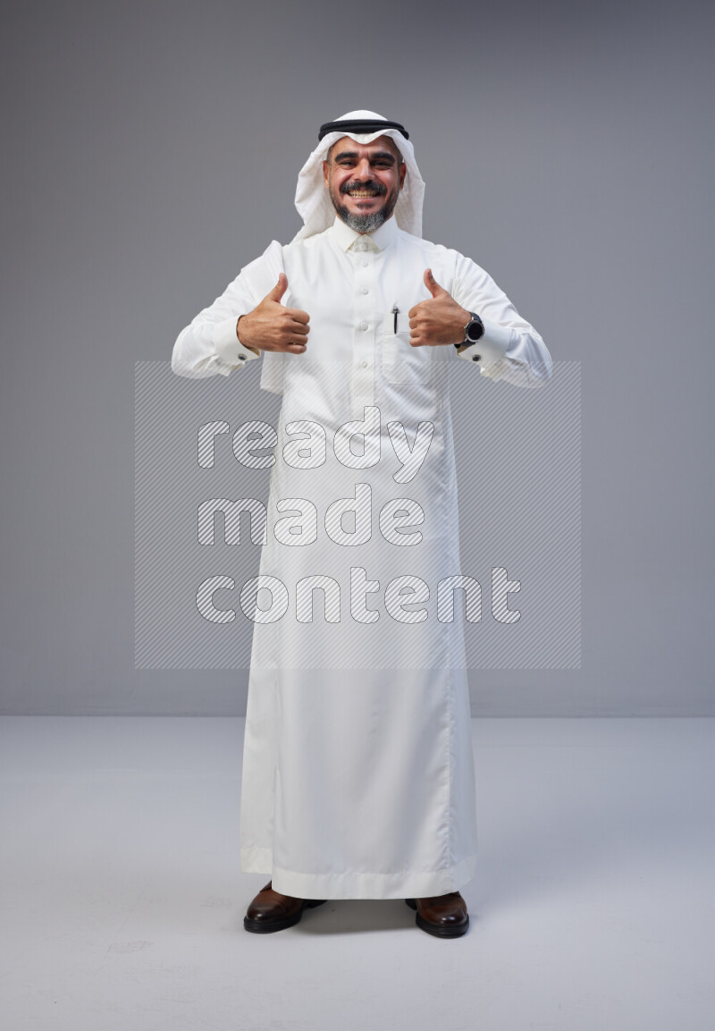 Saudi man Wearing Thob and white Shomag standing interacting with the camera on Gray background