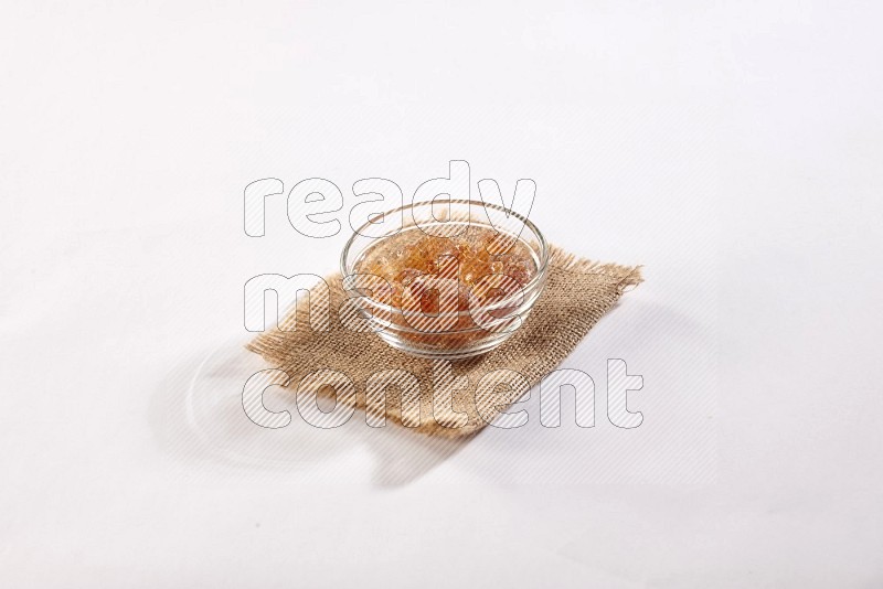 وعاء زجاجي ممتلئ بقطع الصمغ العربي موضوع علي قطعة من قماش الخيش علي خلفية بيضاء