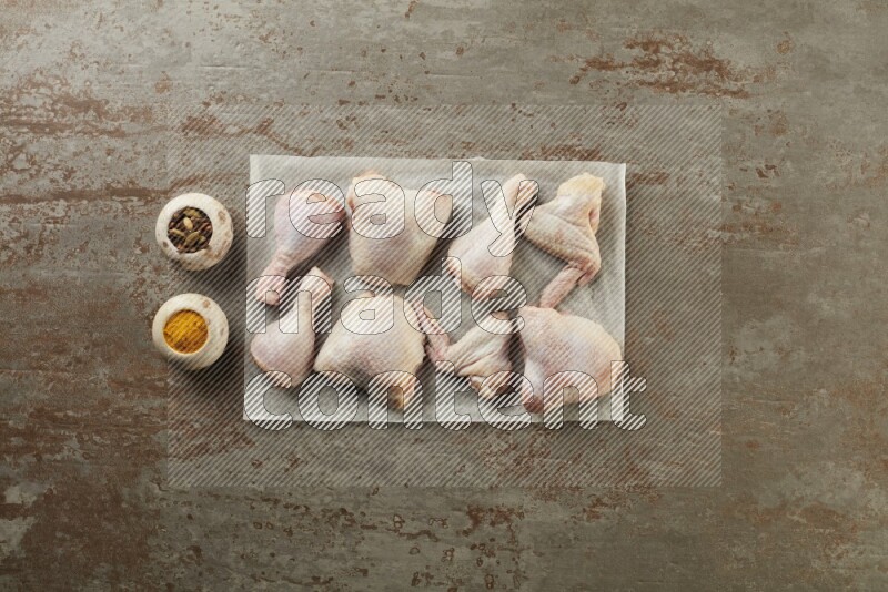 Mixed fresh chicken pieces on a parchment paper direct on a textured rustic background