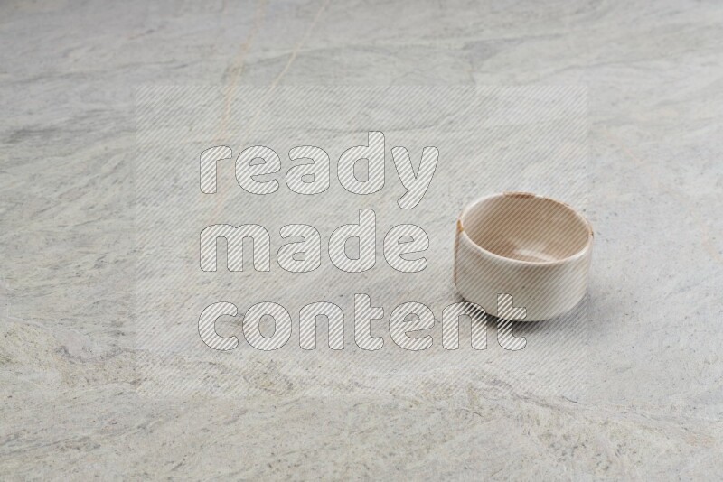 A small beige pottery bowl on grey marble background