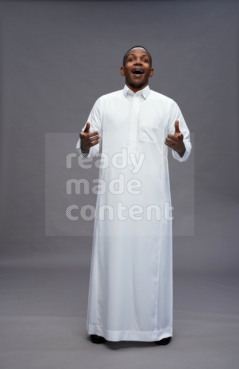 Saudi man wearing thob standing interacting with the camera on gray background