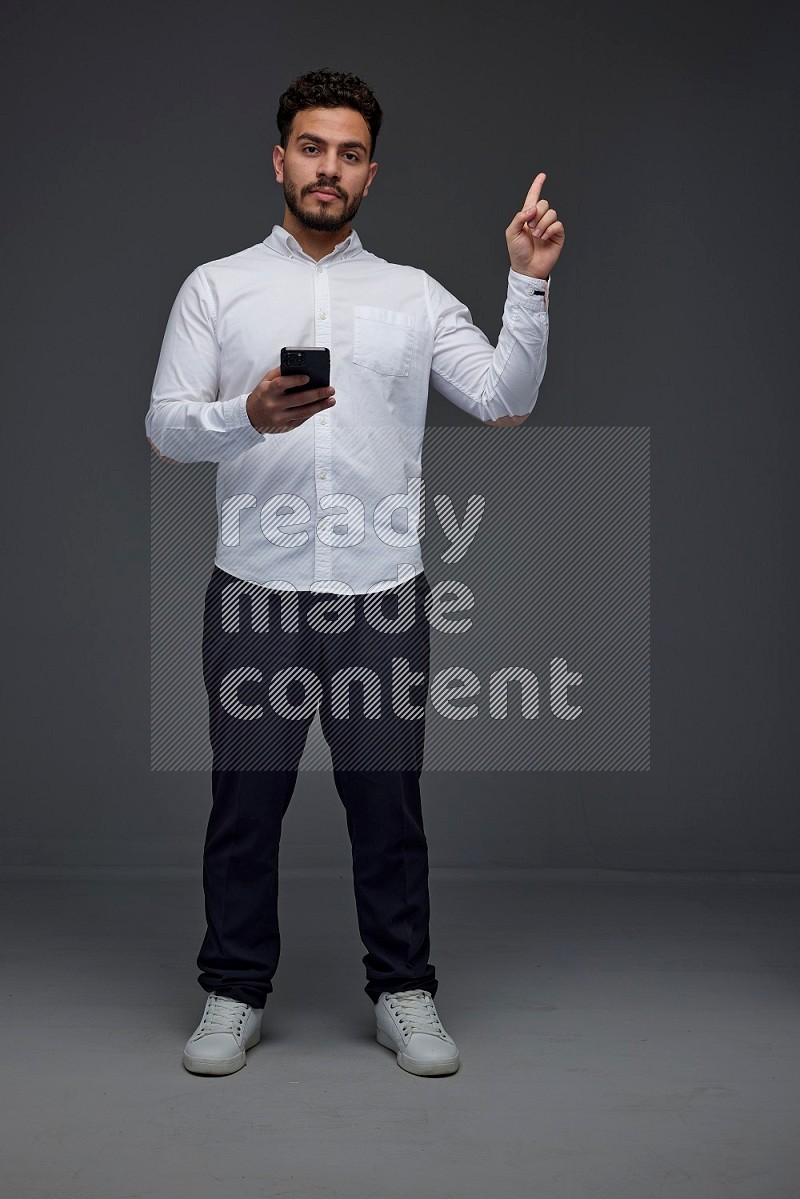 A man wearing smart casual standing and using his phone and making multi hand gestures eye level on a gray background
