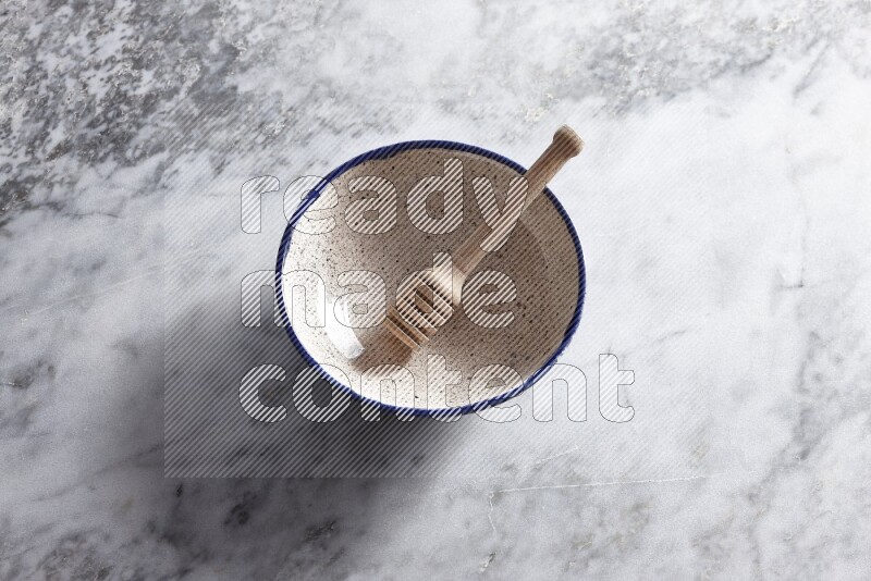 Multicolored pottery bowl with wooden honey dipper in it on grey marble background