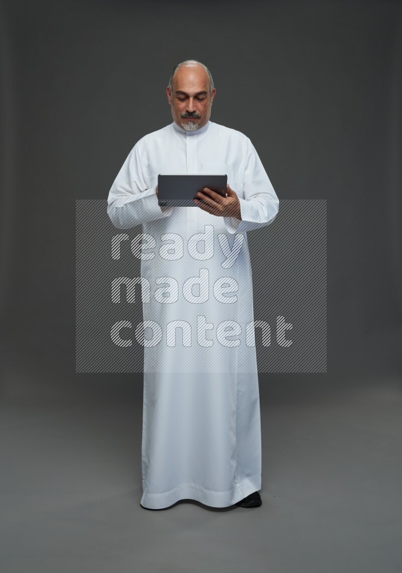 Saudi man without shomag Standing working on tablet on gray background