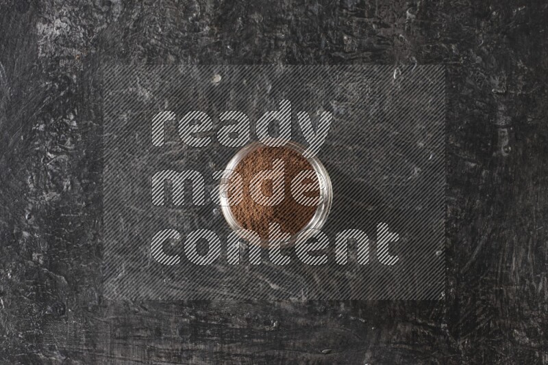 A glass jar full of cloves powder on a textured black flooring