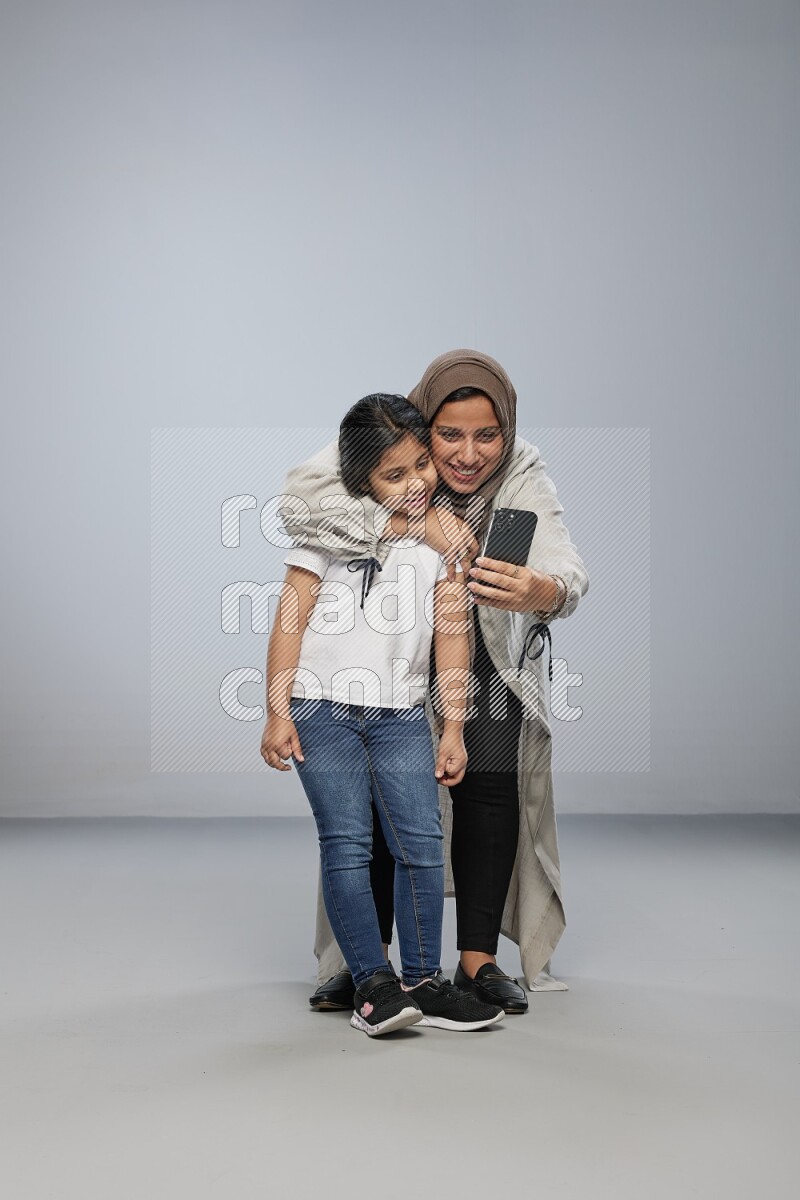A girl standing taking selfie with her mother on gray background