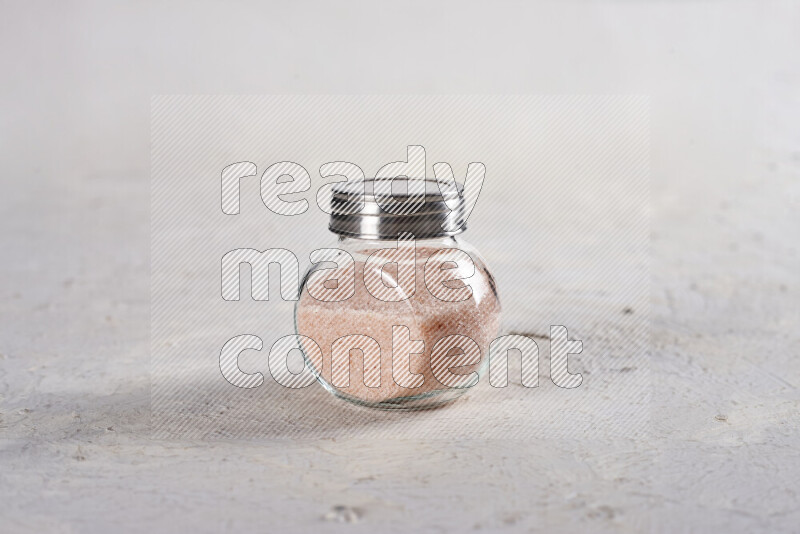 A glass jar full of fine himalayan salt on white background