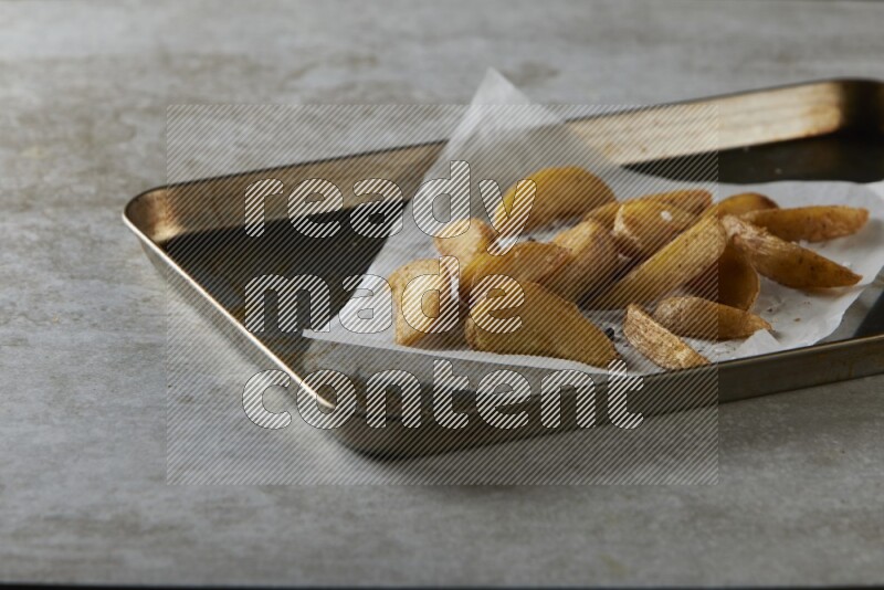 wedges potato on parchment paper in a black stainless steel rectangle tray on grey textured counter top