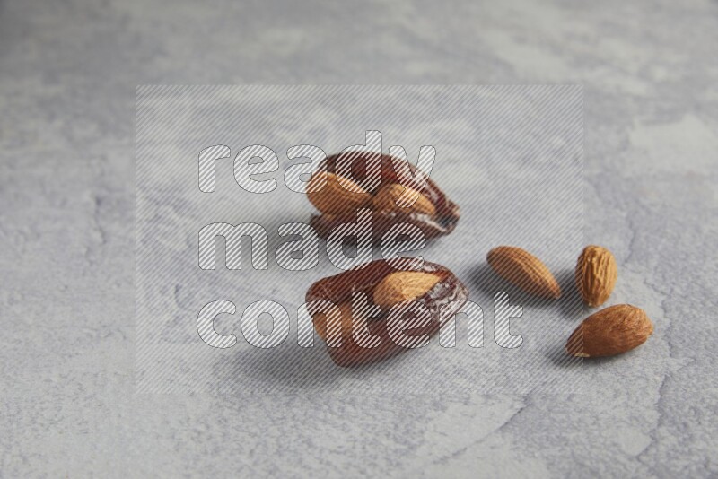 two Almond stuffed date with unroasted  almonds on a light grey background